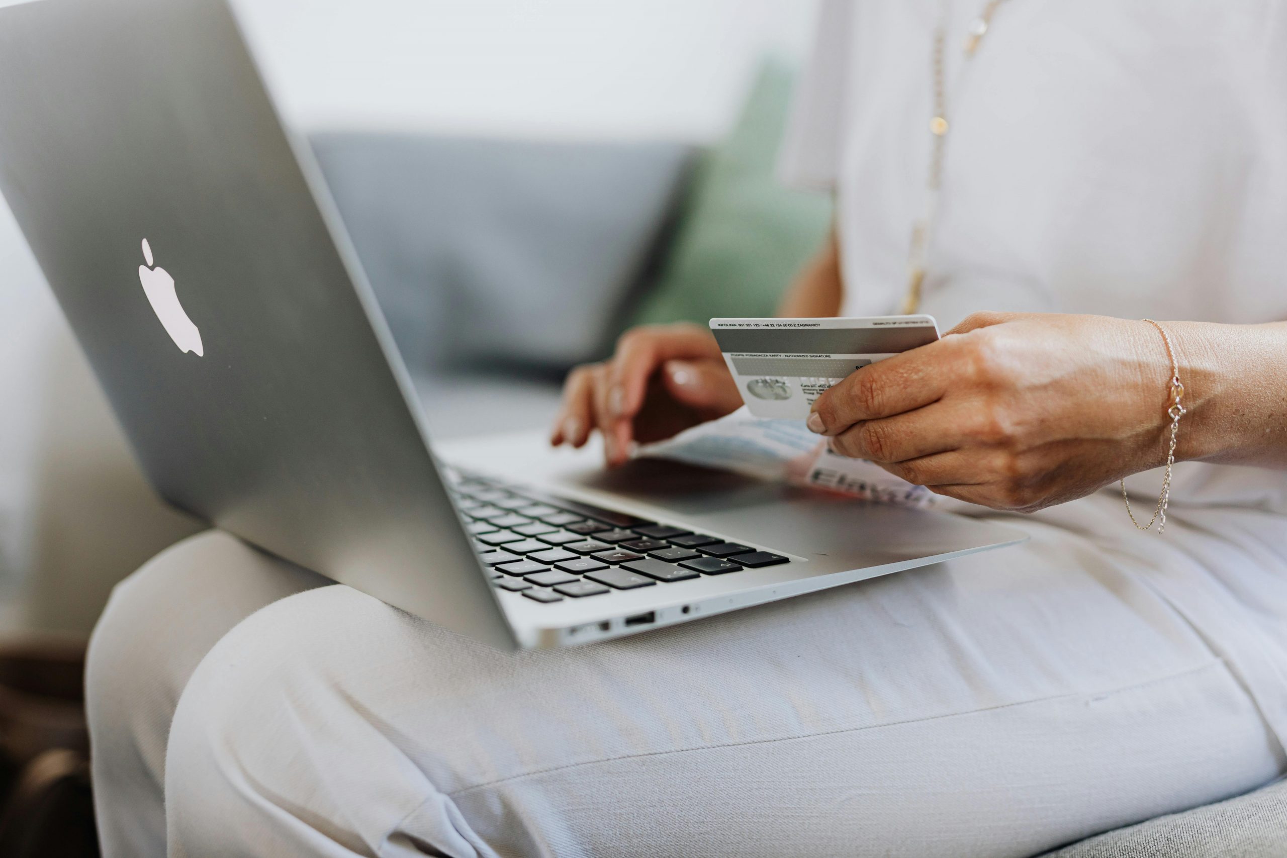 woman with a MacBook on her lap, holding a credit card in one hand